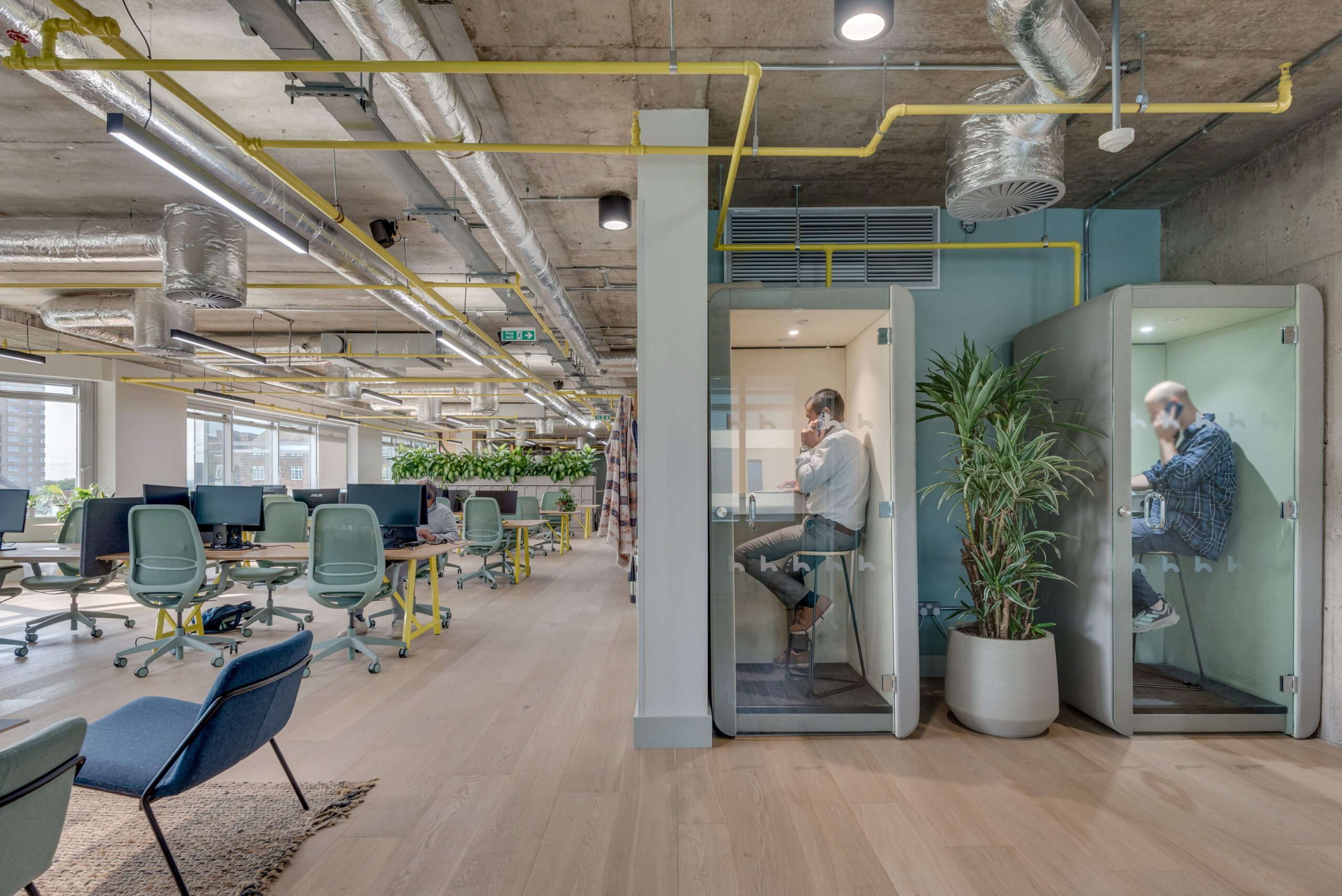 Coworking at Huddle Hammersmith in 3 Shortlands. Two people sat in phonebooths with people working at the desks.