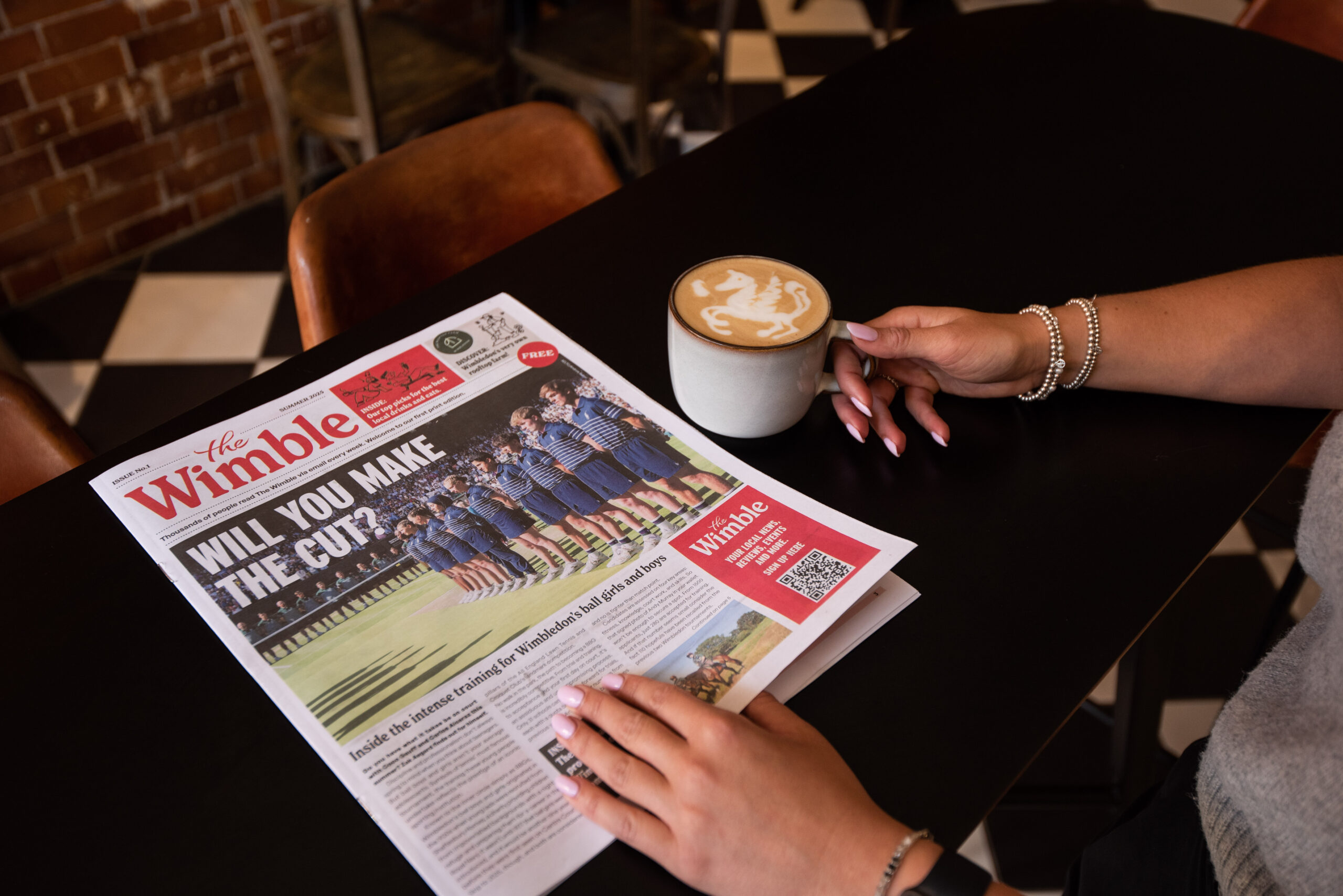 Someone reading The Wimble newspaper whilst drinking a latte with a unicorn on it